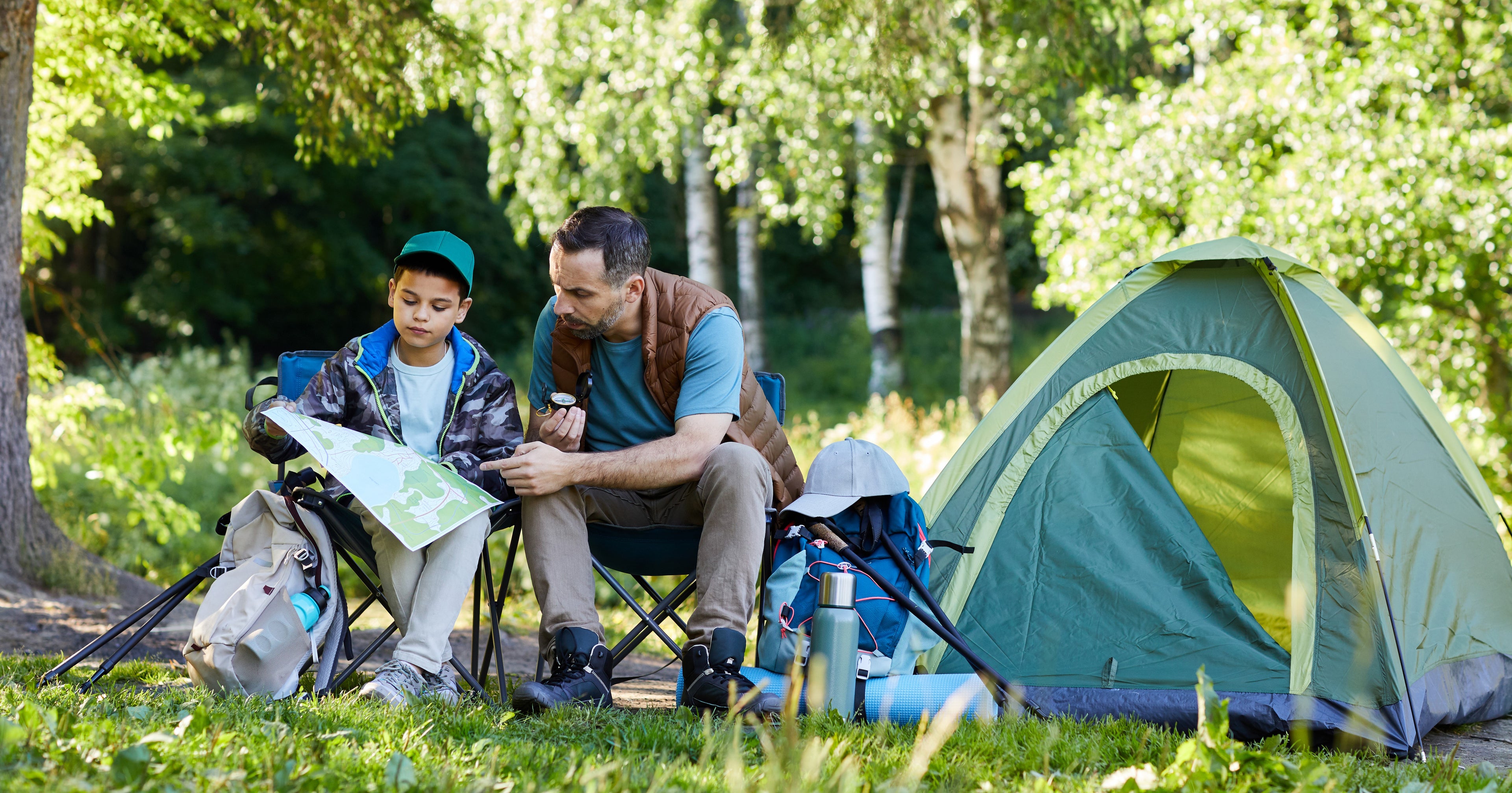 Man and child sitting by a tent in a park, looking at a map.
