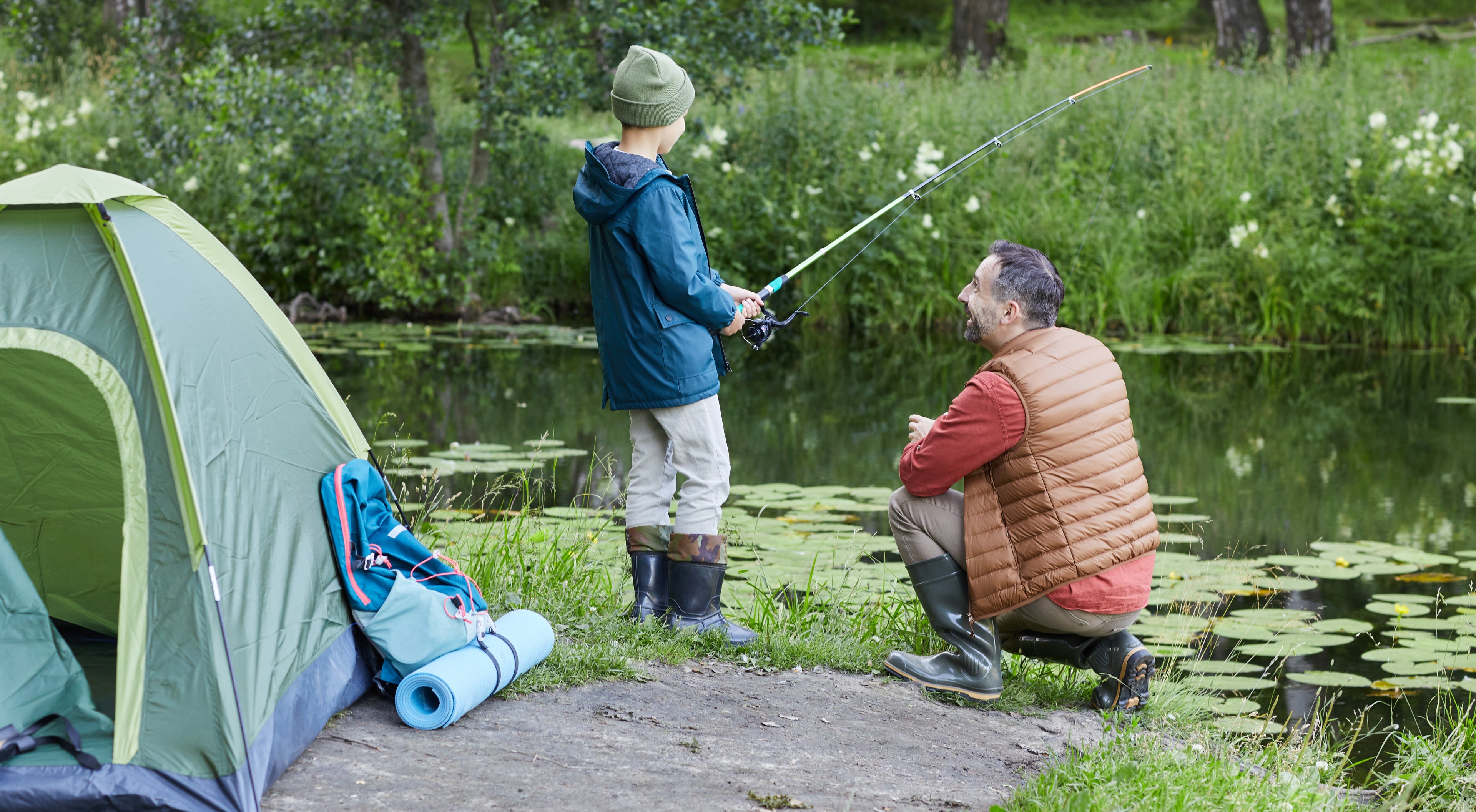 Two people camping by a lake, with one person fishing.